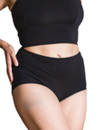 Woman wearing an black high rise organic cotton brief bottom with matching bralette on a white background