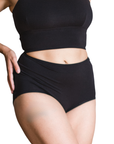 Woman wearing an black high rise organic cotton brief bottom with matching bralette on a white background