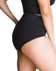 Woman wearing an black high rise organic cotton brief bottom on a white background, side view