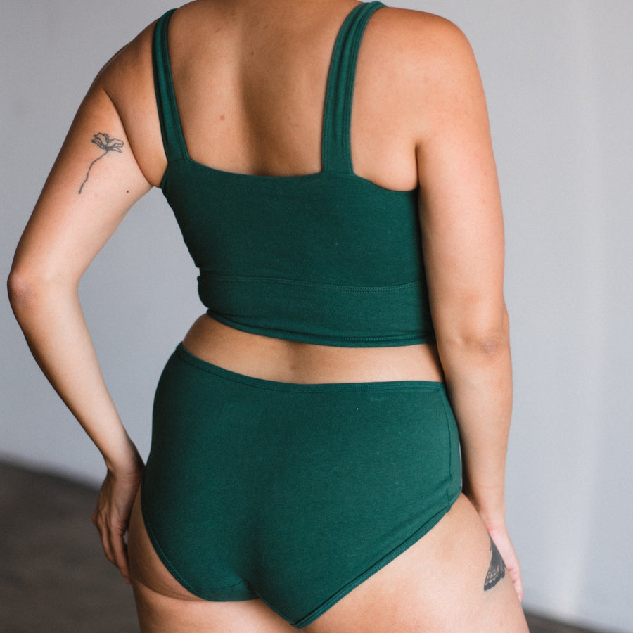 back view of model in square neck bralette and matching mid rise briefs in lagoon, a dark teal green color.