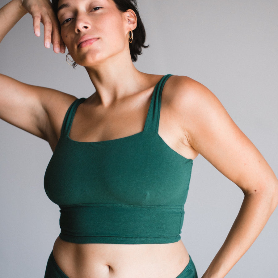 front view with model hand grazing side of head wearing lagoon sustainable organic cotton and hemp square neck bralette with matching briefs. lagoon is a dark greenish teal color.