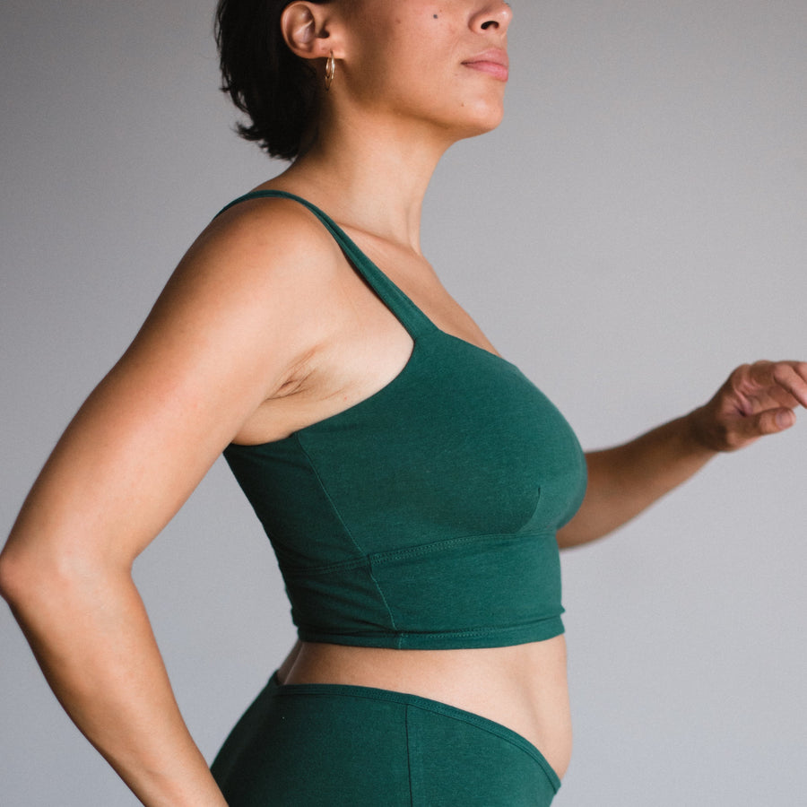 side view of model wearing square neck bralette and mid rise briefs in lagoon, a dark green teal color.