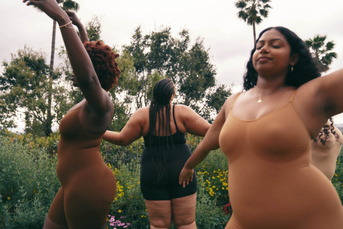 PROCLAIM inclusive nude plant based shapewear on models dancing in a lush green outdoor setting