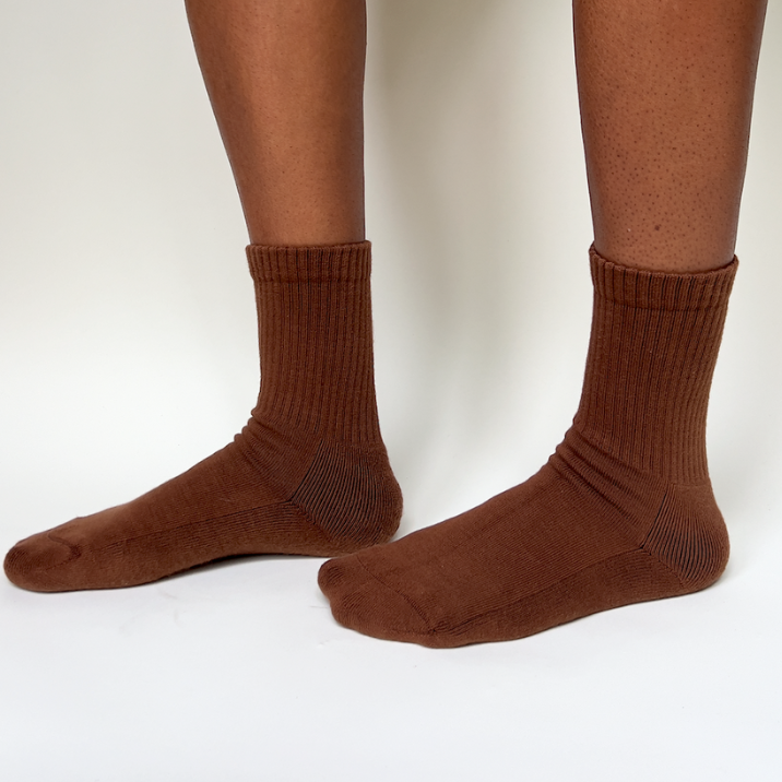 Model wearing a pair of organic pima cotton crew socks that are ethically and sustainably made in Peru. In Ella, a warm brown tone.