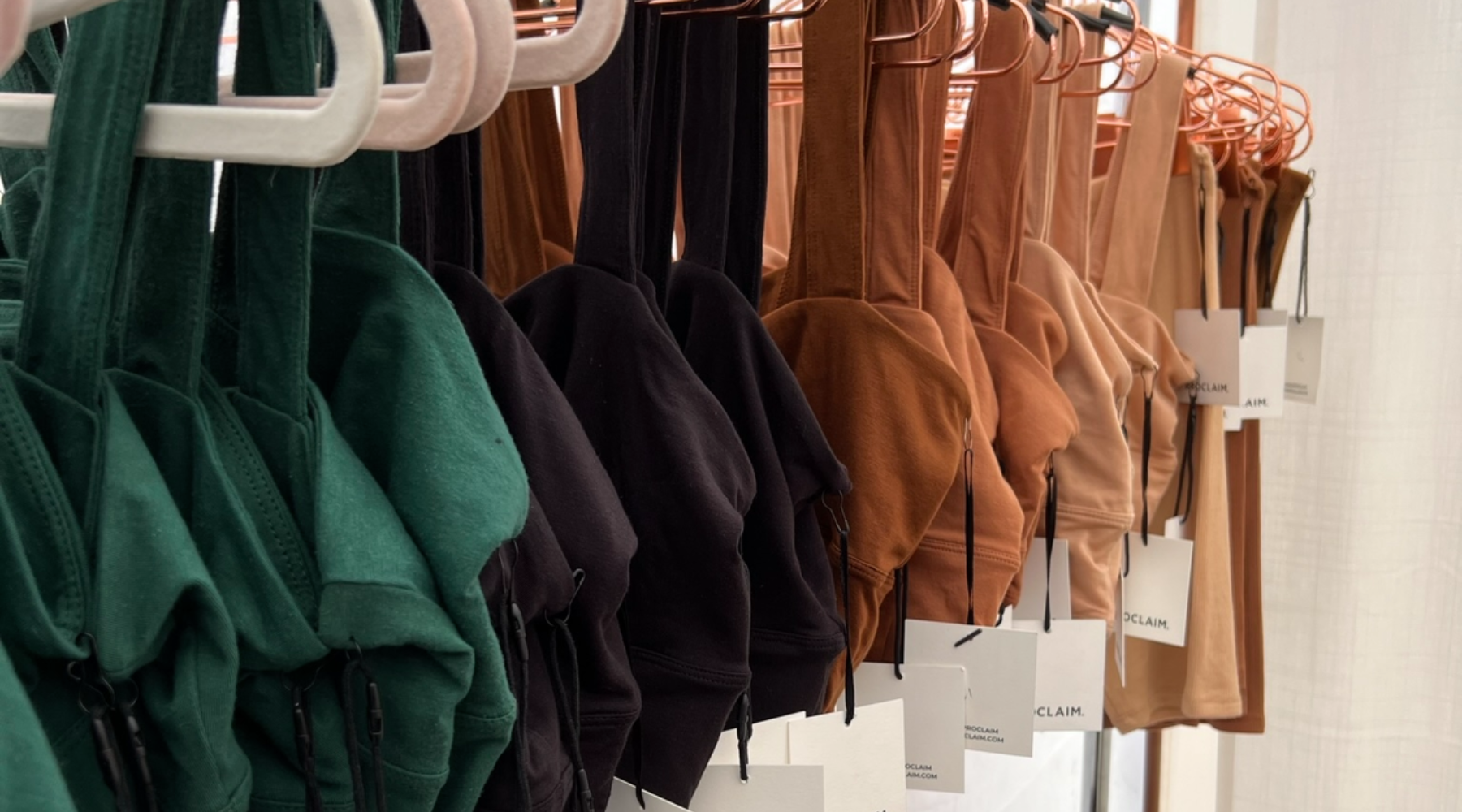 a rack of proclaim bras in green, black and inclusive nude tones in organic cotton with  hang tags