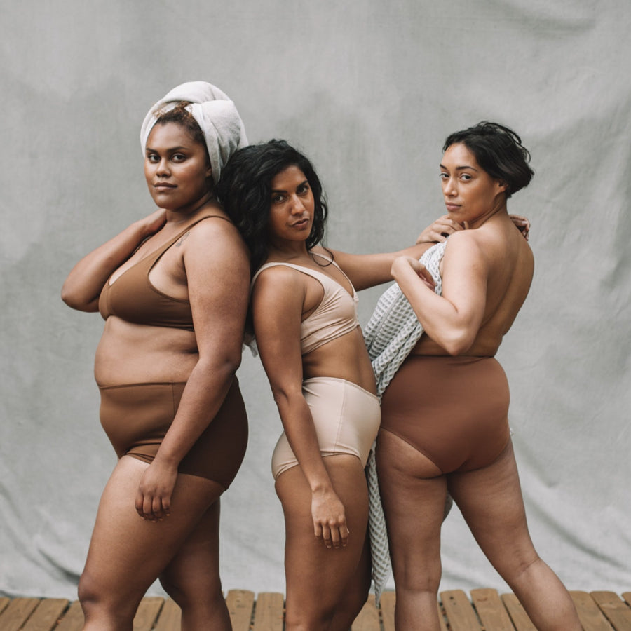 Three models in PROCLAIM Ella, Maya and Ada Nude swim sets with towels.