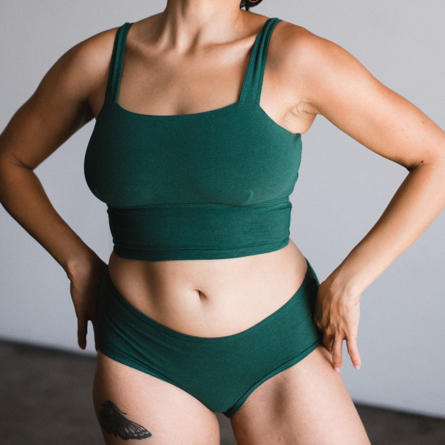 model with hands on hip wearing sutainable organic cotton and hemp square neck bralette with matching mid rise briefs in lagoon, a dark green teal color.