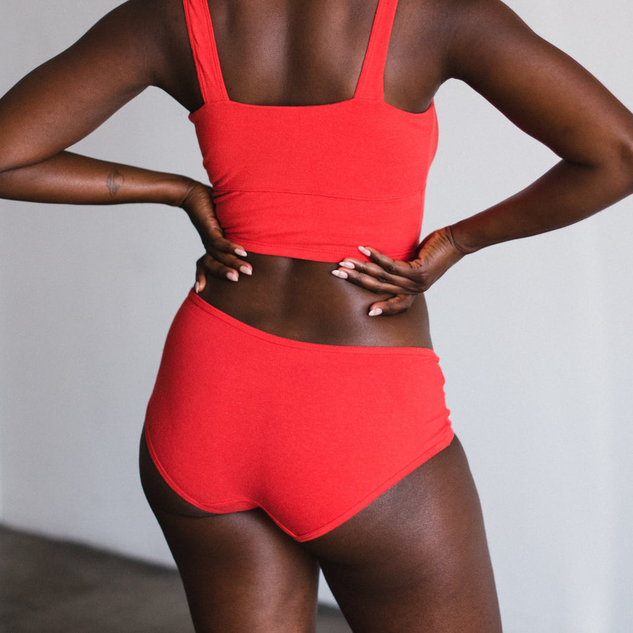 model with hips on hand wearing mid rise briefs in poppy a bright red color made from organic cotton and hemp