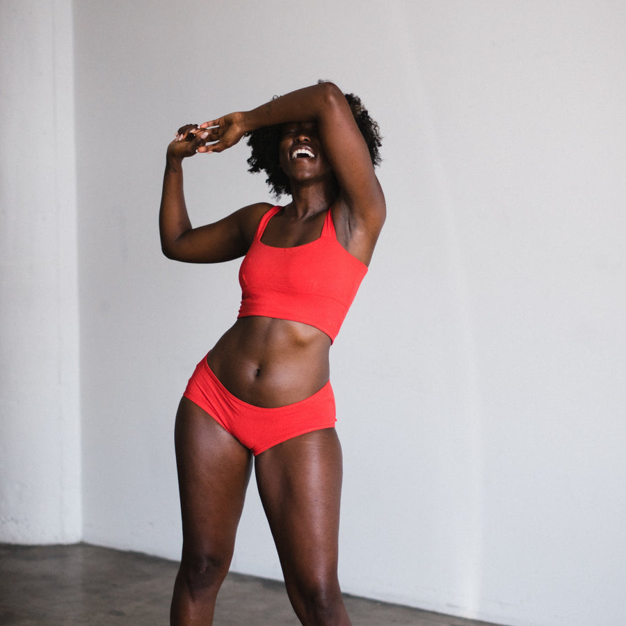 model with hand covering eyes laughing wearing red poppy square neck bralette and mid rise briefs in matching color